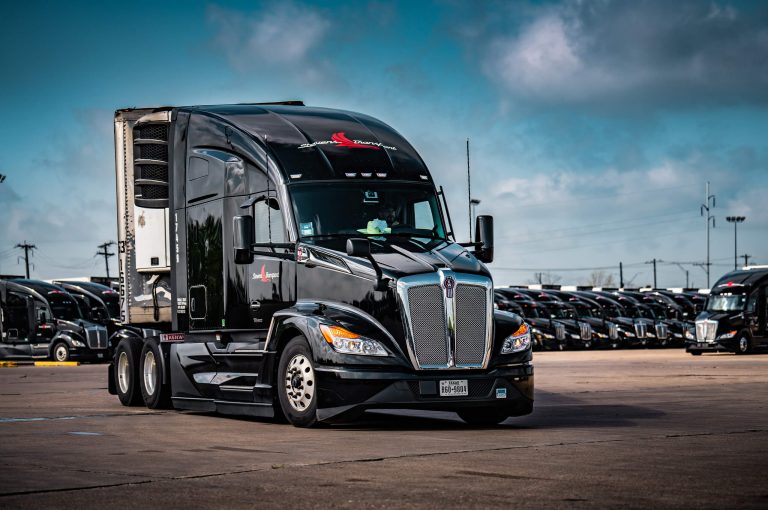 Image of Stevens truck driving in parking lot, other Stevens trucks parked in a line behind