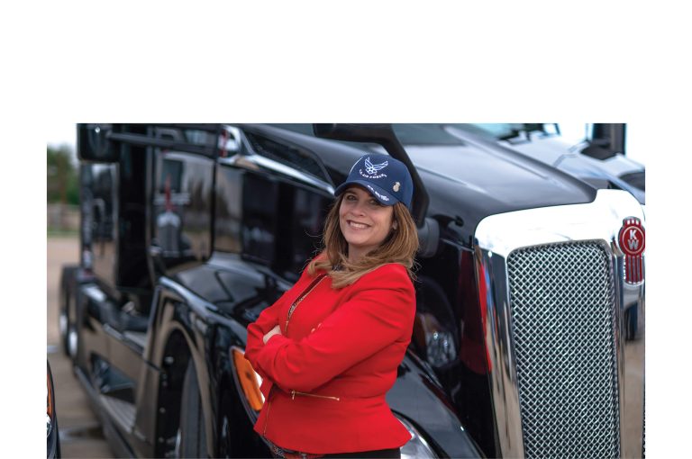 Image of veteran woman wearing hat, standing in front of black truck with arms crossed