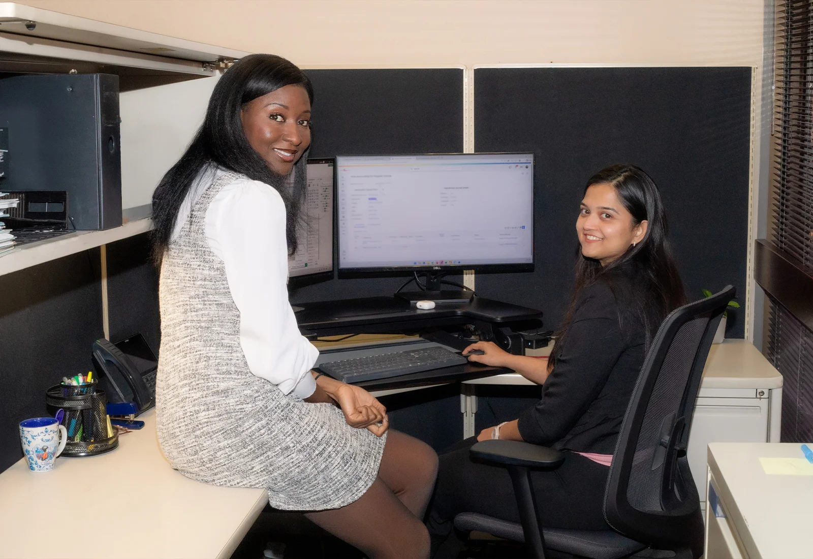 Two smiling interns sitting in a cubicle with a computer monitor